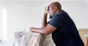 man with eyes closed standing against moving boxes