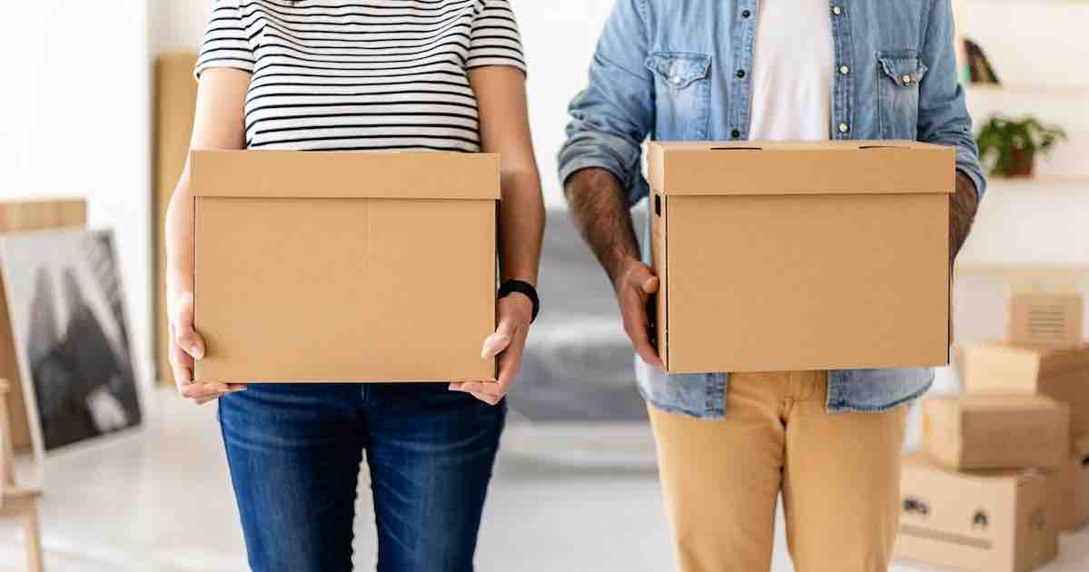 Young couple carrying cardboard boxes while considering professional storage.