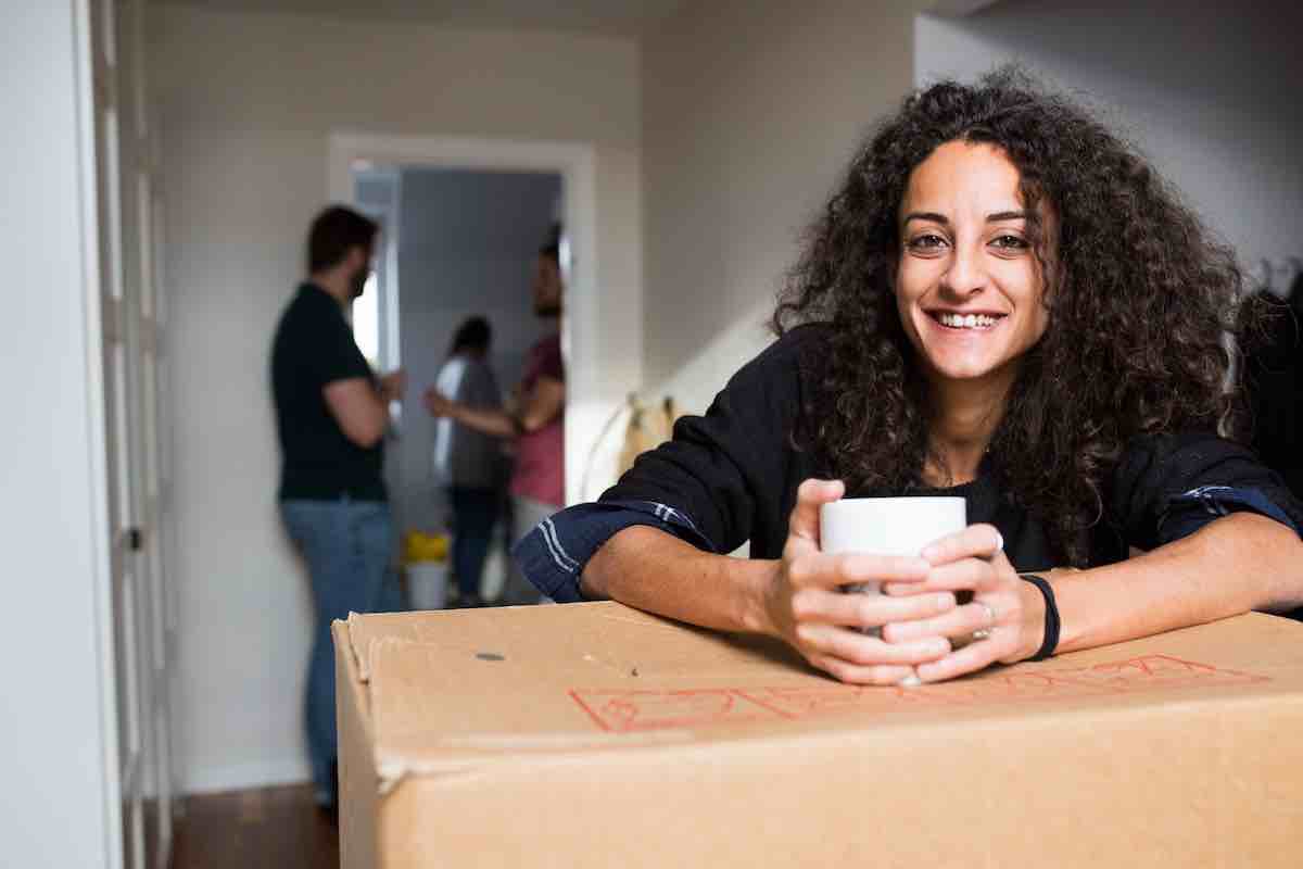 Happy woman leaning on a box, relaxing after working through her moving checklist PDF.