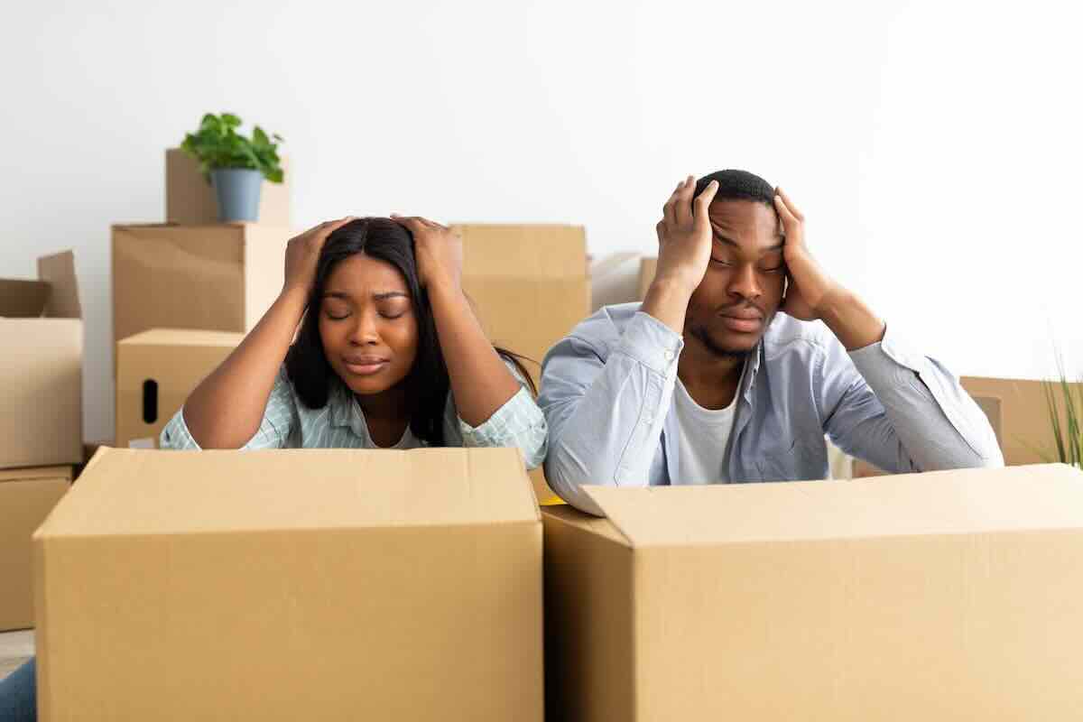 Frustrated African American couple sitting with moving boxes after hiring moving brokers.