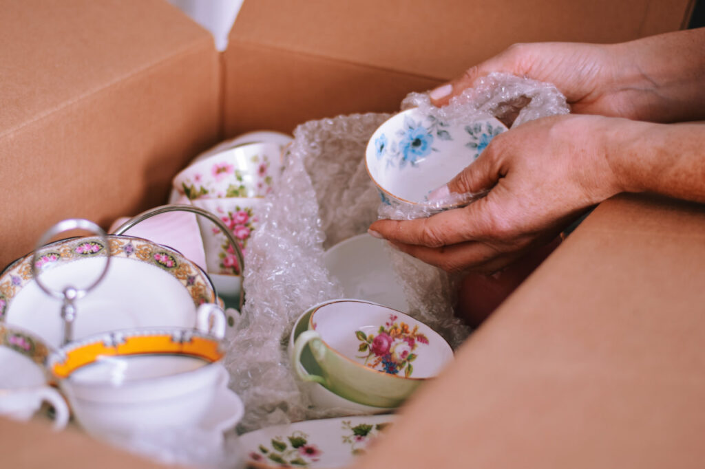 Close up of a person packing china cups while moving with aging parents and providing caregiving during a move.