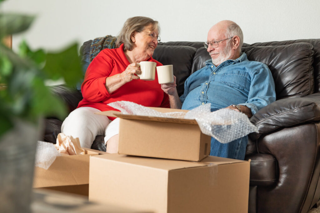 Happy elderly couple drinking coffee on the couch after following senior relocation tips for moving with aging parents.