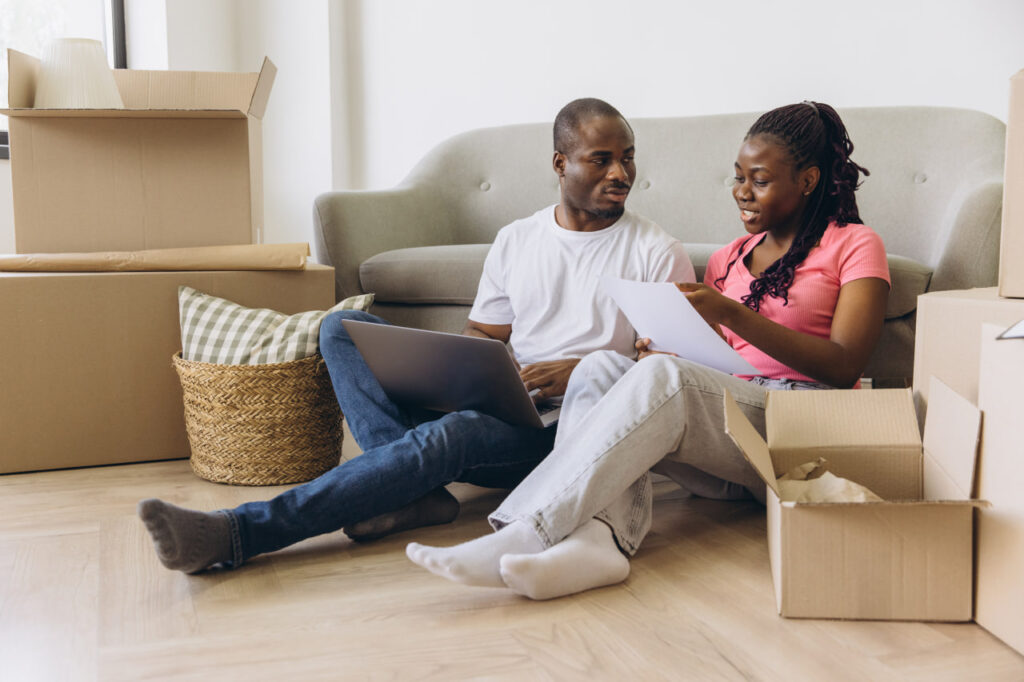 Man and wife sitting on the floor while managing finances after relocation to account for the cost of living after moving.