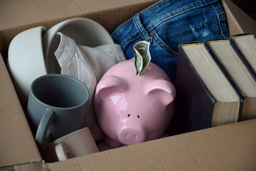 A piggybank with a dollar is in a box, representing the need for post-move budgeting.