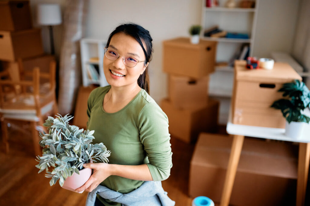 Smiling young woman holding a plant who has calculated her new cost of living after moving through post-move budgeting.