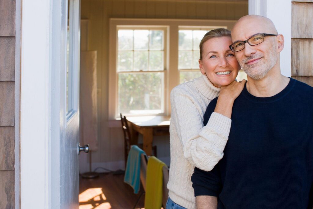 Happy middle-aged couple in front of their new home who know how how to save money on a professional move.